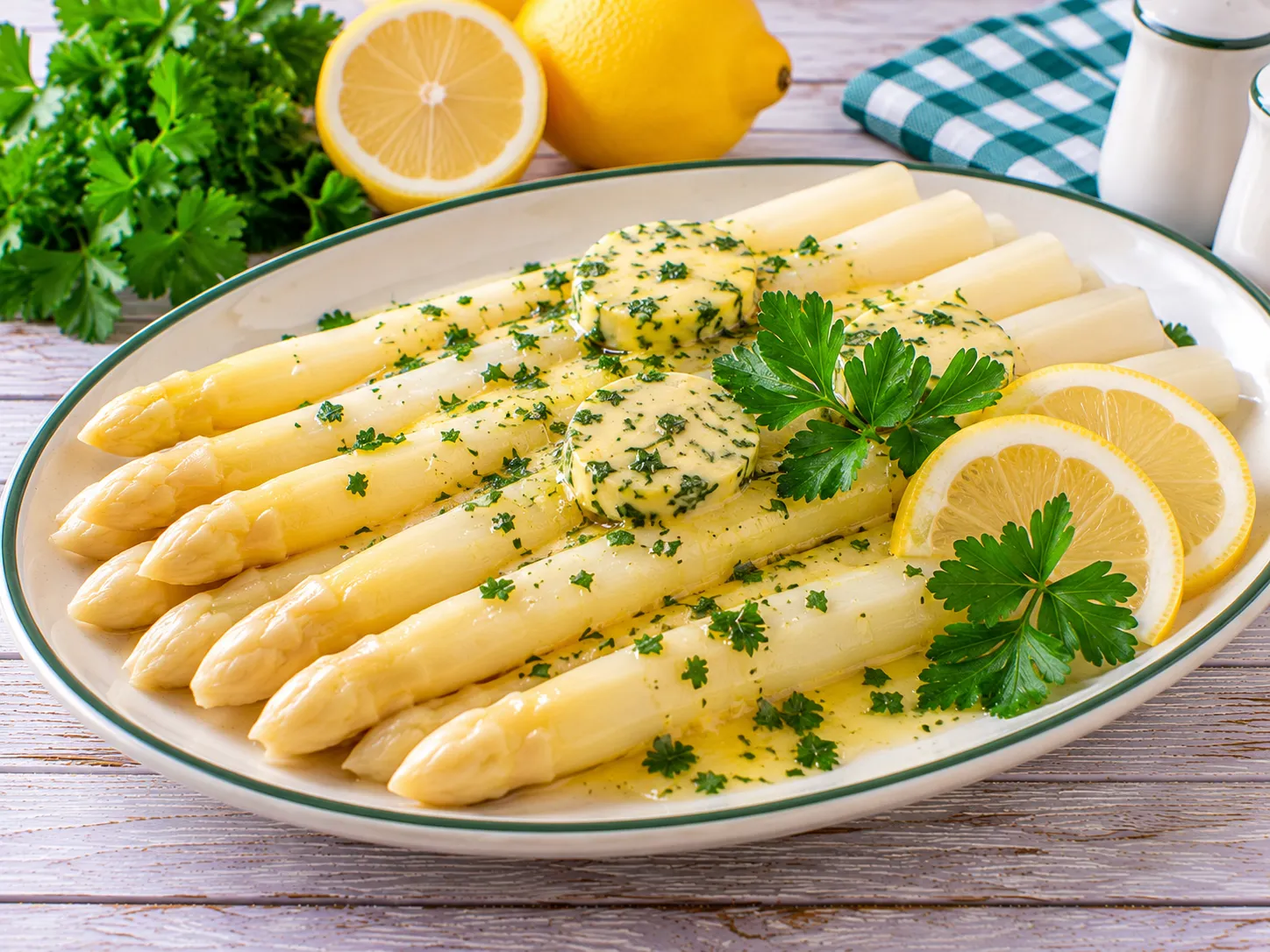 Weiße Spargelspitzen mit Kräuterbutter, Zitronenscheibe und Petersilie.