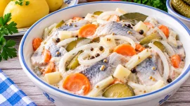 Marinierte Heringe mit Zwiebeln, Gurken, Möhren, Apfel und cremiger Soße.