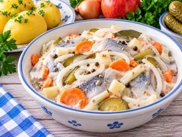 Marinierte Heringe mit Zwiebeln, Gurken, Möhren, Apfel und cremiger Soße.