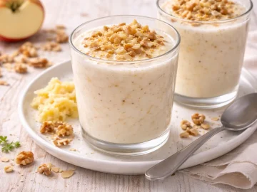 Glas mit Apfel-Milch-Dessert und geriebenem Apfel auf hellem Holztisch angerichtet