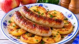 Goldbraune Bratwürstchen auf gebratenen Apfelscheiben aus der Pfanne.