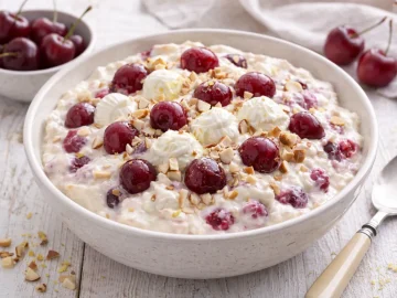 Quarkspeise mit Kirschen und Mandeln in einer weißen Schüssel auf weißem Holzhintergrund