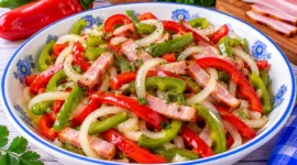 Peperonisalat aus roten und grünen Peperoni mit geräuchertem Speck und Zwiebeln.