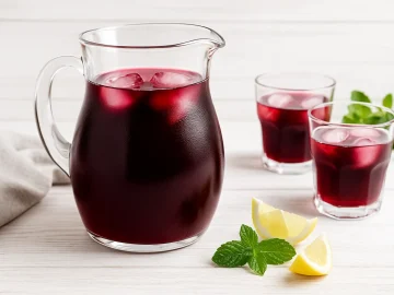 Glaskrug mit Rotwein-Tee-Bowle, serviert mit Gläsern und frischer Deko auf Holztisch