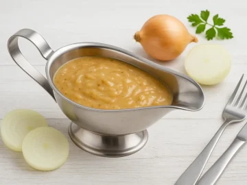 Zwiebelsoße in eleganter Edelstahlsauciere, serviert auf Holztisch mit frischen Zwiebeln und Petersilie