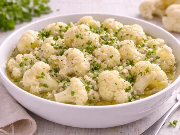 Blumenkohlsalat mit Marinade in weißer Schüssel auf hellem Holzhintergrund