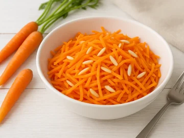 Weiße Schüssel mit Karottensalat und Mandeln auf weißem Holzhintergrund, dekoriert mit frischen Karotten