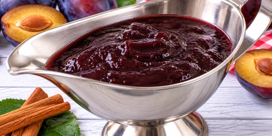 Dunkle Powidelsoße aus Pflaumenmus mit Zimt und Rum in einer Sauciere aus Edelstahl.