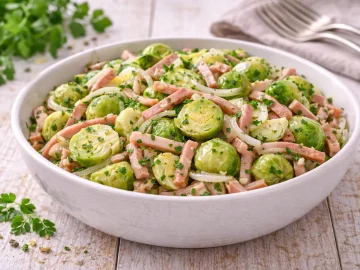 Rosenkohlsalat mit Schinkenstreifen und Petersilie in moderner Salatschüssel auf hellem Holztisch