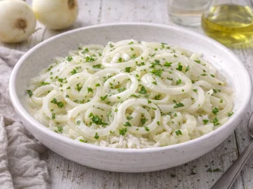 Zwiebelsalat aus blanchierten Zwiebelringen mit Kräutern in weißer Schüssel auf weißem Holzhintergrund