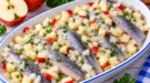 Heringsfilets mit gewürfelten Äpfeln und Zwiebeln in einer hellen Servierschale.