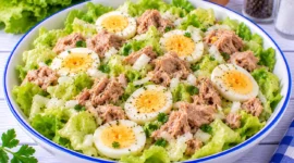 Frischer Kopfsalat mit Thunfischstücken, Eierscheiben und fein geschnittenen Zwiebeln.