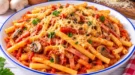 Lange Makkaroni in Tomatensoße mit Schinkenstreifen, Pilzen und geriebenem Käse.