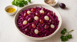 Rotkohlsalat mit Weintrauben und Einmachzwiebeln in heller Schüssel auf weißem Holzhintergrund