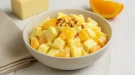 Fruchtiger Ananas-Käse-Salat mit Mandeln in heller Schale auf weißem Holzhintergrund