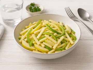 Birnensalat mit Käse und grüner Paprika in weißer Schüssel auf weißem Holztisch