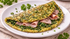 Gefaltetes Omelette mit Spinat und Schinken auf weißem Teller serviert