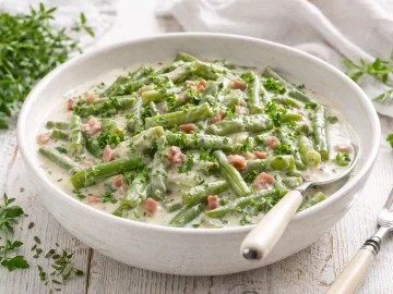 Grüne Bohnen in cremiger Specksoße mit Petersilie in einer weißen Schüssel auf weißem Holzhintergrund