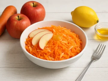 Apfel-Möhren-Salat in einer weißen Schüssel mit geriebenen Möhren, Apfelstücken und Honig