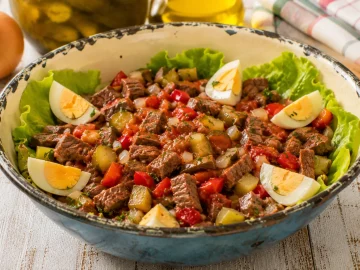 Pikanter Rindfleischsalat mit Letscho, Gewürzgurken und Ei in einer Emaille-Schüssel mit Gebrauchsspuren.